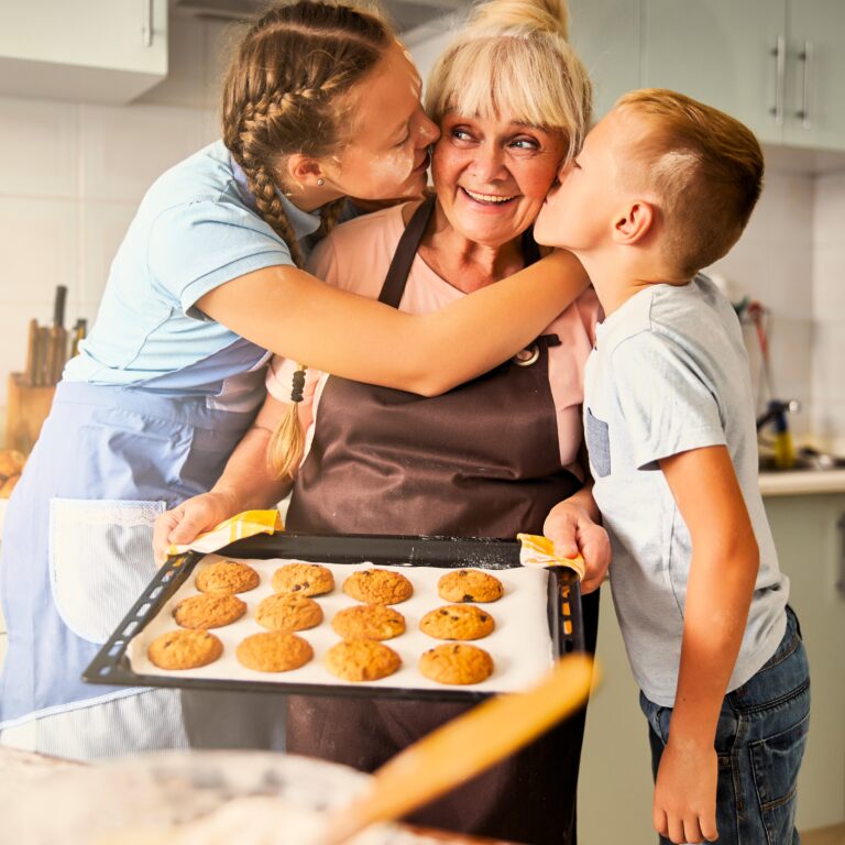 Blissful grandma baking cookies being kissed by thankful children